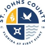 St Johns County logo with a circular design featuring a seashell, a bird, waves, and a geometric symbol Text reads “St Johns County, Florida at First Sight, Est ”